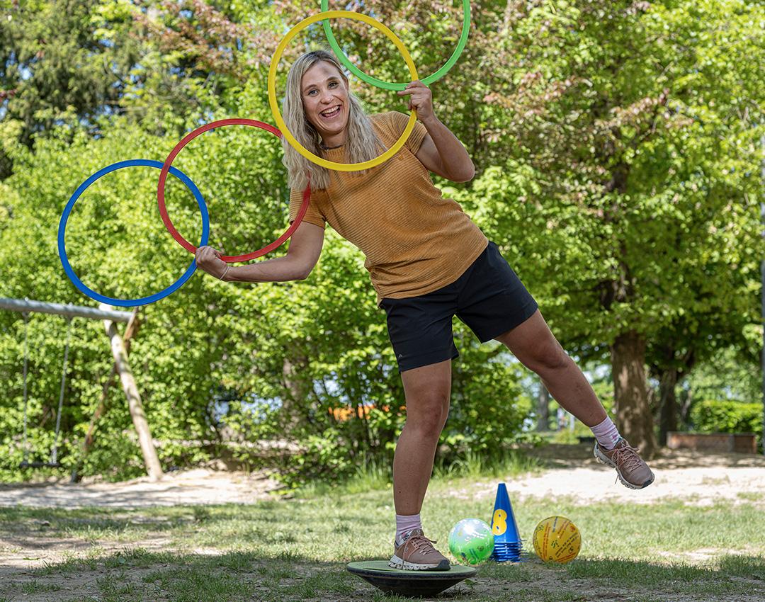 Junge Frau im Grünen turnt mit Hula Hoop Reifen.